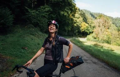 Lachende Frau steht mit dem Fahrrad auf einer Landstraße im Grünen.