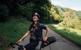 Lachende Frau steht mit dem Fahrrad auf einer Landstraße im Grünen.