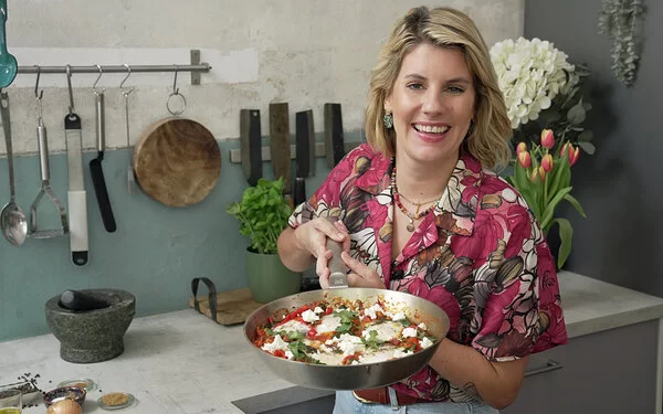 Felicitas Then hält eine eiserne Pfanne mit würziger Shakshuka mit beiden Händen in Richtung Kamera.