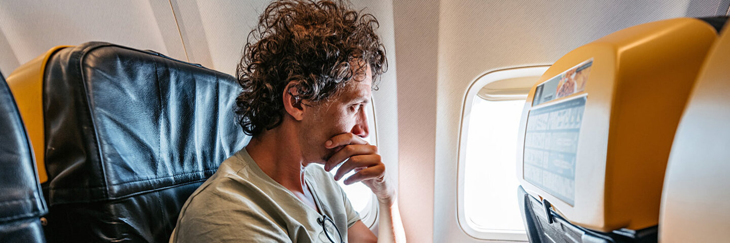 Ein mittelalter Mann sitzt im Flugzeug und schaut ängstlich aus dem Fenster.