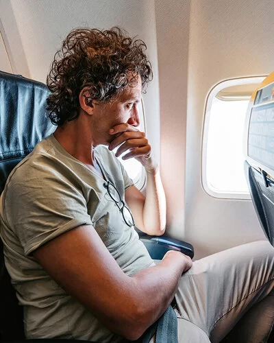 Ein mittelalter Mann sitzt im Flugzeug und schaut ängstlich aus dem Fenster.