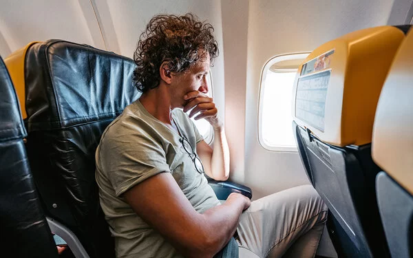 Ein mittelalter Mann sitzt im Flugzeug und schaut ängstlich aus dem Fenster.