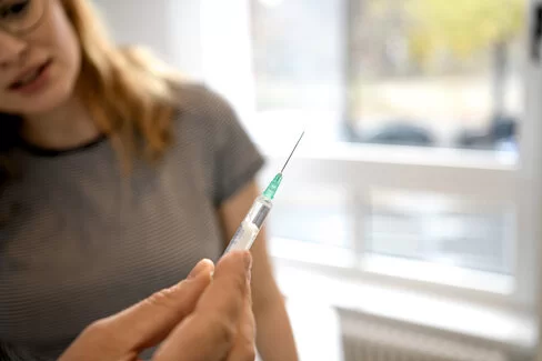 Ein Arzt hält eine Spritze in der Hand. Er wird damit eine Patientin impfen.