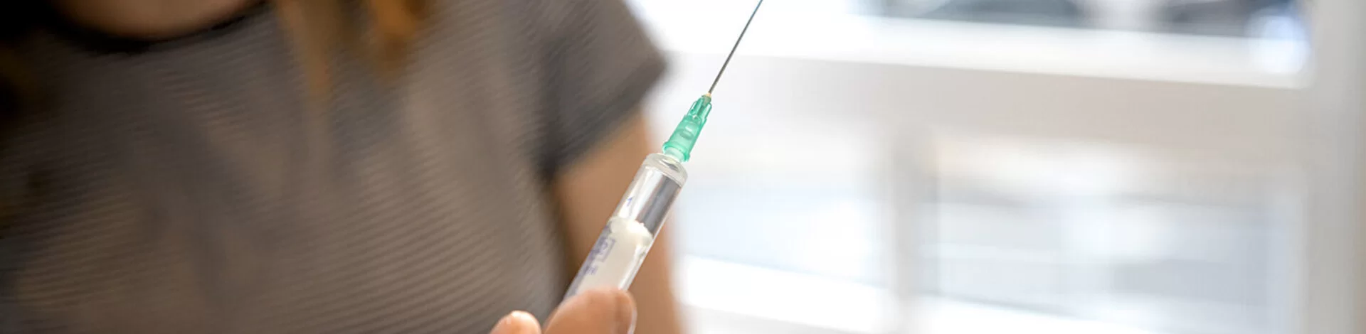 Ein Arzt hält eine Spritze in der Hand. Er wird damit eine Patientin impfen.