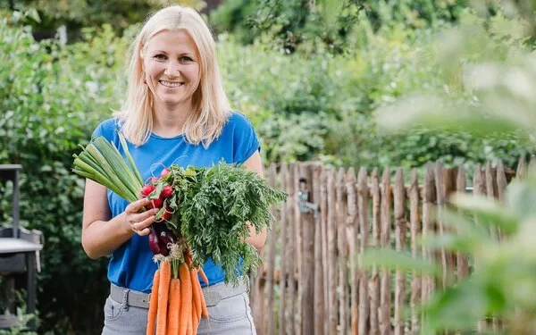 Jenny Böhme steht in einem Garten und hält frisch geerntetes Gemüse in den Händen.