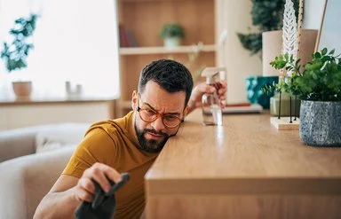 Ein mittelalter Man reinigt akkurat und mit kritischem Blick einen Tisch mit Tuch und Spray.
