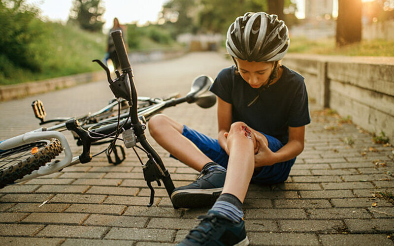 Ein Junge ist mit dem Fahrrad gestürzt und schaut sich die Wunde am Knie an.