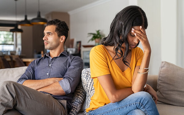 Ein Mann und eine Frau sitzen voneinander abgewandt auf der Couch – sie sind unglücklich in ihrer Beziehung.