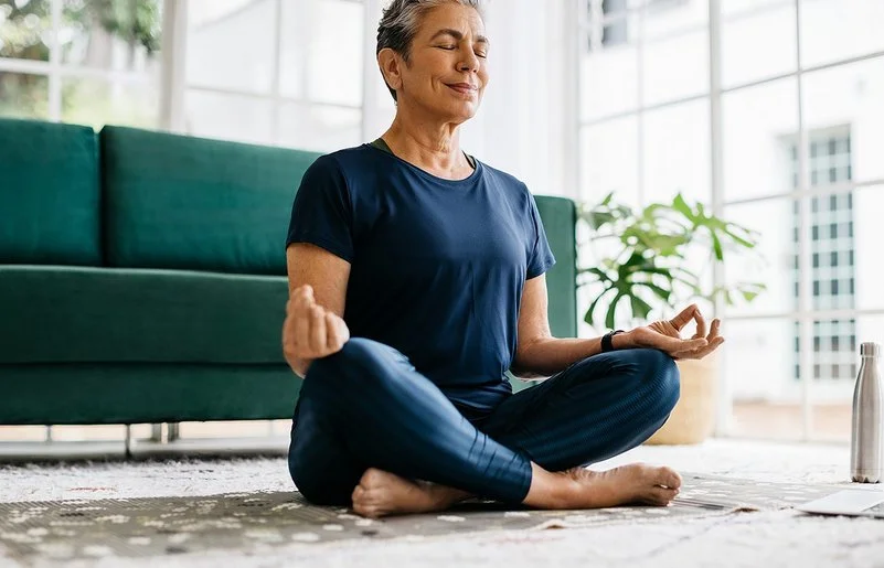 Eine Seniorin sitzt mit geschlossen Augen im Schneidersitz.