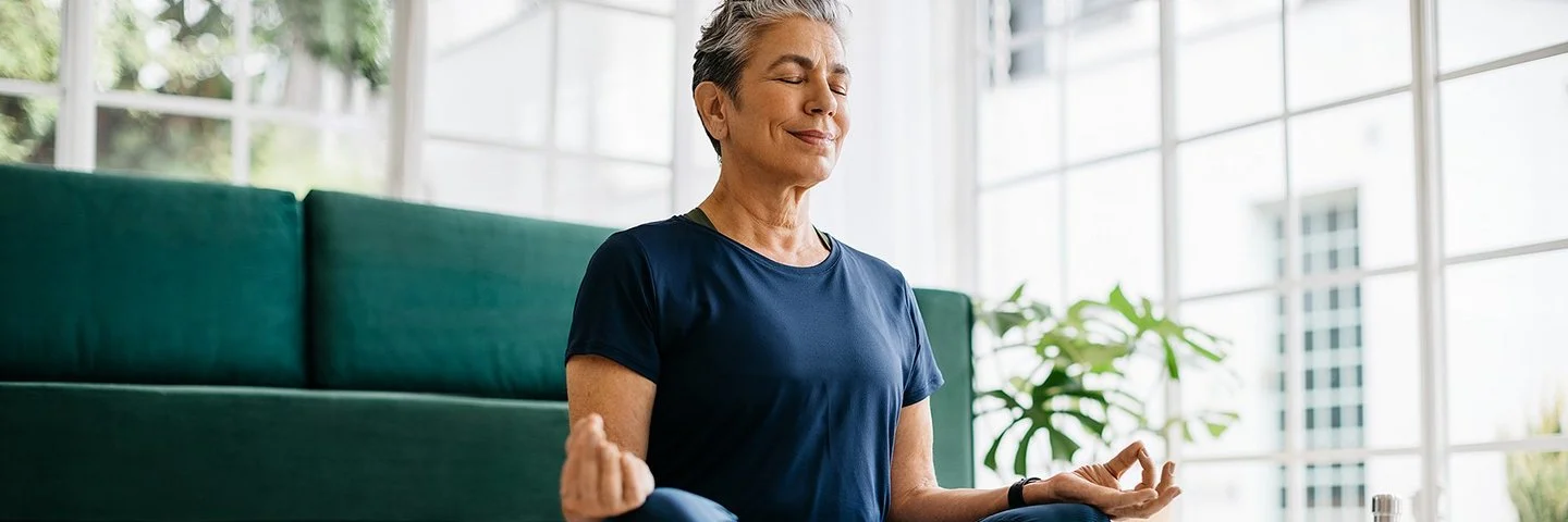 Eine Seniorin sitzt mit geschlossen Augen im Schneidersitz.