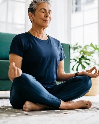 Eine Seniorin sitzt mit geschlossen Augen im Schneidersitz.