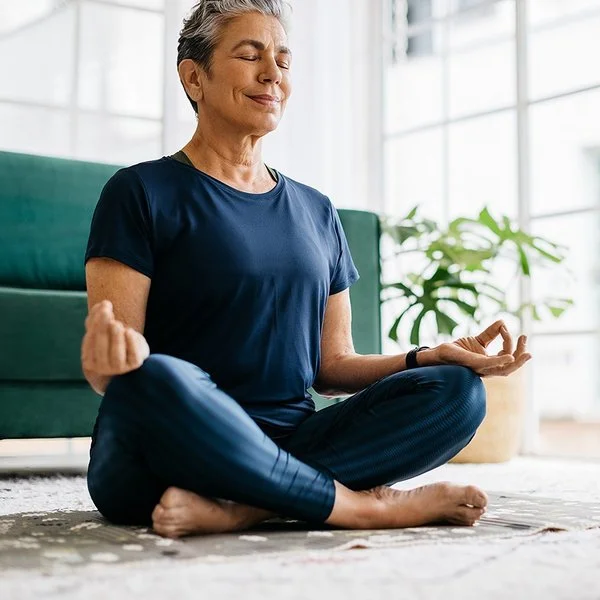 Eine Seniorin sitzt mit geschlossen Augen im Schneidersitz.