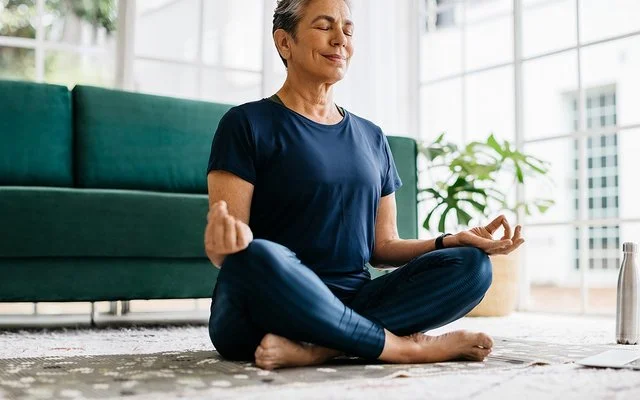 Eine Seniorin sitzt mit geschlossen Augen im Schneidersitz.