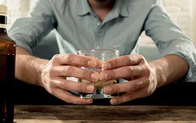 Mann sitzt auf der Couch und schaut auf ein Glas mit Alkohol.