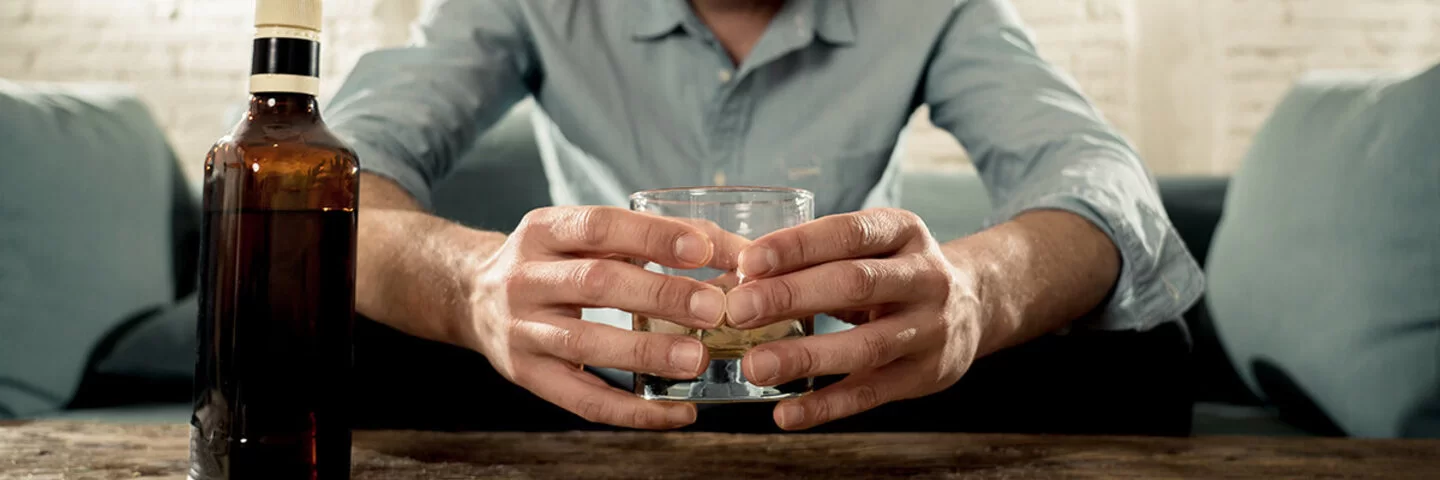 Mann sitzt auf der Couch und schaut auf ein Glas mit Alkohol.