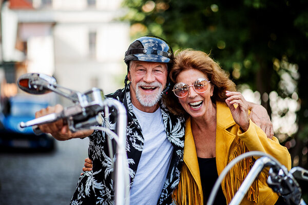 Ein fröhliches Seniorenpaar mit Motorrad und Sonnenbrillen in der Stadt.