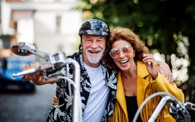 Ein fröhliches Seniorenpaar mit Motorrad und Sonnenbrillen in der Stadt.