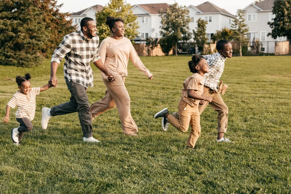 Ein Mann, eine Frau und drei Kinder laufen lachend über eine Wiese.