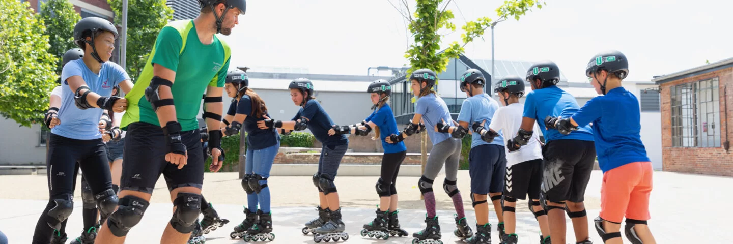 Eine Menschengruppe fährt auf Inlineskates in einer Schlange auf einem Gebäudehof.