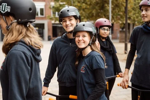 Eine Gruppe Kinder und Jugendlicher sthen bekleidet mit schwarzen T-Shirts und Helmen auf einem Vorplatz.