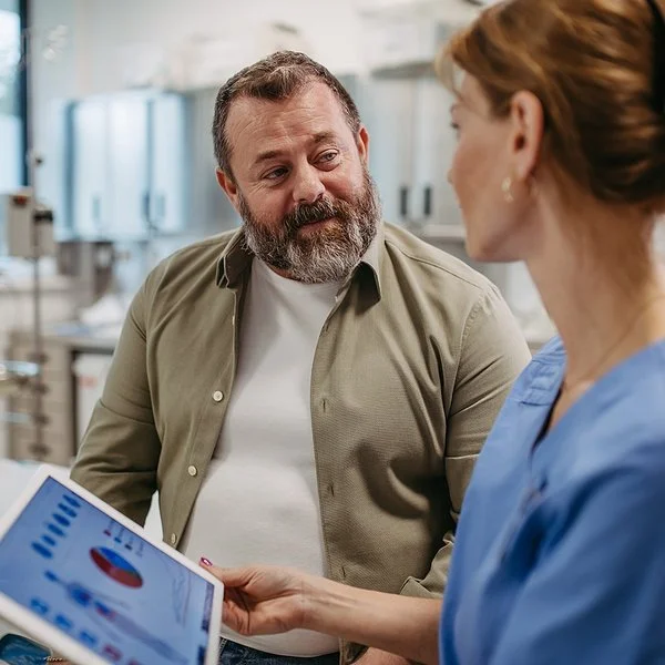 Eine Ärztin hält ein Tablet in der Hand und spricht mit einem Patienten.