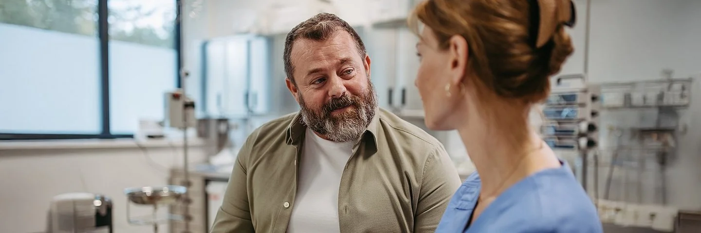 Eine Ärztin hält ein Tablet in der Hand und spricht mit einem Patienten.