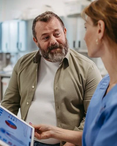 Eine Ärztin hält ein Tablet in der Hand und spricht mit einem Patienten.
