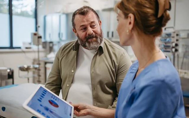 Eine Ärztin hält ein Tablet in der Hand und spricht mit einem Patienten.
