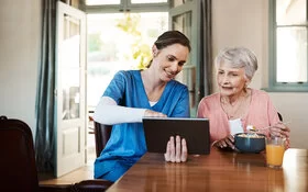 Eine Pflegekraft zeigt einer älteren Dame ihre Gesundheitswerte auf dem Tablet.