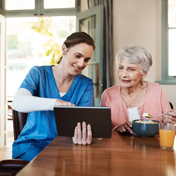 Eine Pflegekraft zeigt einer älteren Dame ihre Gesundheitswerte auf dem Tablet.