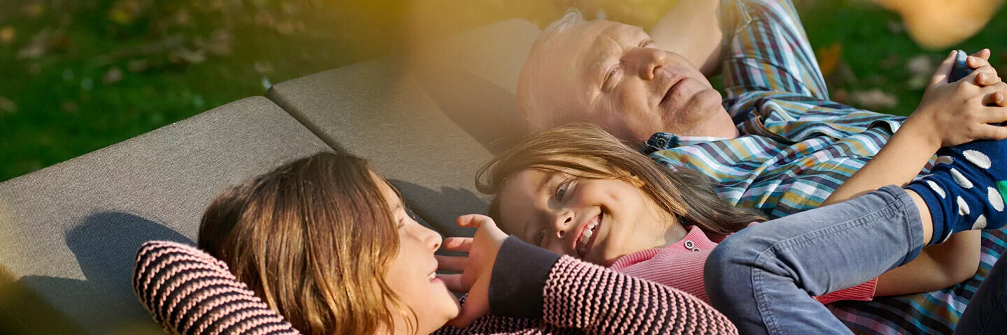 Zwei Kinder und ein älterer Mann liegen in der Sonne. Mit dem Familiencoach Krebs können sie gemeinsam besser mit der Krebserkrankung umgehen.