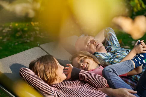 Zwei Kinder und ein älterer Mann liegen in der Sonne. Mit dem Familiencoach Krebs können sie gemeinsam besser mit der Krebserkrankung umgehen.