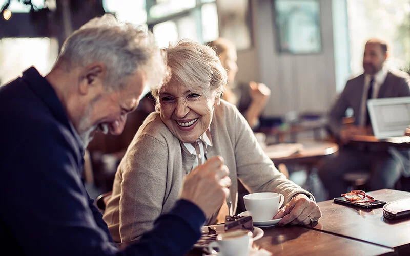 Ein älteres Paar sitzt im Café und unterhält sich lachend.