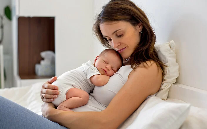 Eine Mutter kuschelt mit ihrem neugeborenen Baby im Wochenbett.