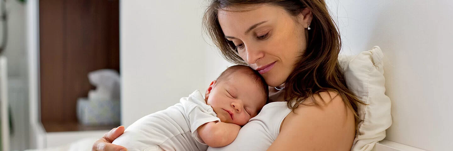 Eine Mutter kuschelt mit ihrem neugeborenen Baby im Wochenbett.