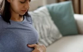 Eine schwangere Frau mit Schwangerschaftsbeschwerden hält sich den Bauch und den Rücken 