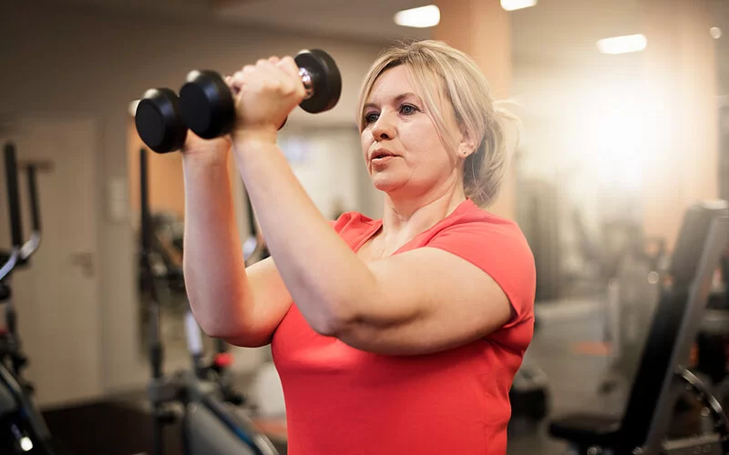 Eine Frau trainiert ihre Arme mit Hanteln im Fitnessstudio.