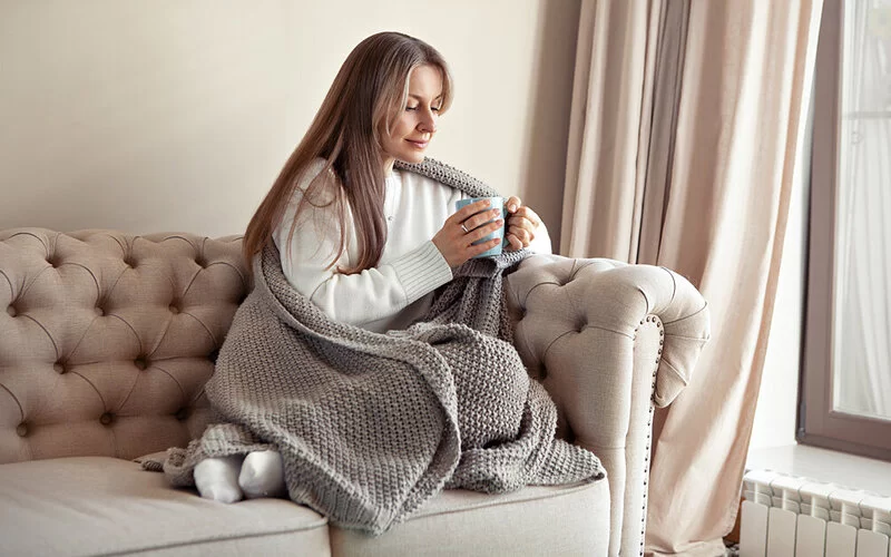 Eine Frau sitzt auf dem Sofa und trinkt einen Tee aus Mönchspfeffer.