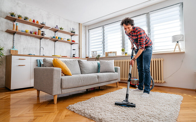 Mann nutzt Natron zum Putzen, indem er es über seinen Teppich streut und absaugt.