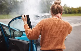 Eine Frau hat bei einem Autounfall ein Schleudertrauma erlitten und hält sich mit einer Hand den Nacken.