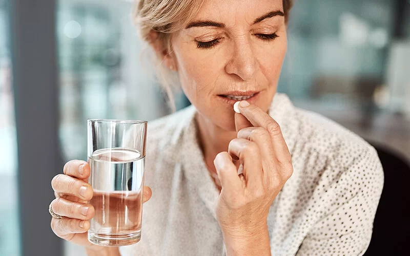 Eine Frau hält eine Tablette in der einen und ein Glas Wasser in der anderen Hand.