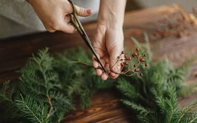 Eine Person schneidet Beeren und Zweige für einen selbst gemachten Adventskranz.