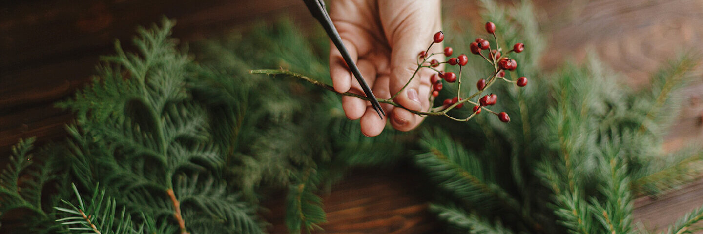 Eine Person schneidet Beeren und Zweige für einen selbst gemachten Adventskranz.