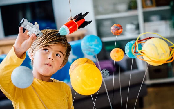 Ein Junge hält einen Astronautenfigur in der Hand und lernt spielerisch mit einem Modell des Sonnensystems.