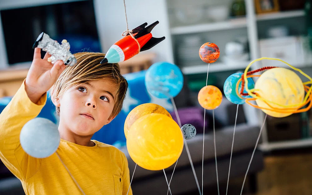 Ein Junge hält einen Astronautenfigur in der Hand und lernt spielerisch mit einem Modell des Sonnensystems.