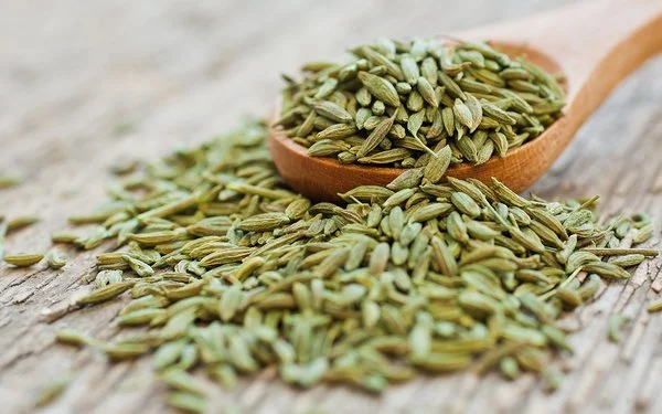 Anissamen liegen auf einem Holzlöffel und auf einem Tisch.