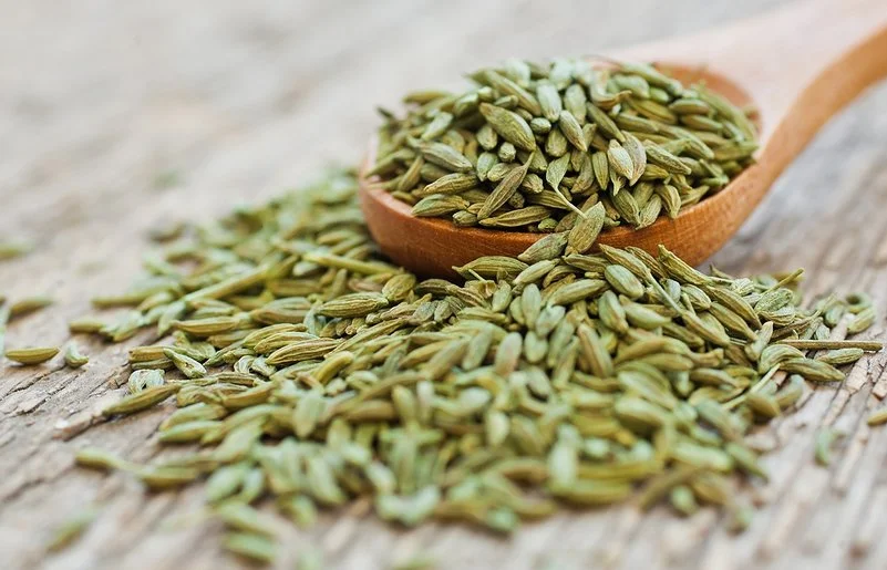 Anissamen liegen auf einem Holzlöffel und auf einem Tisch.