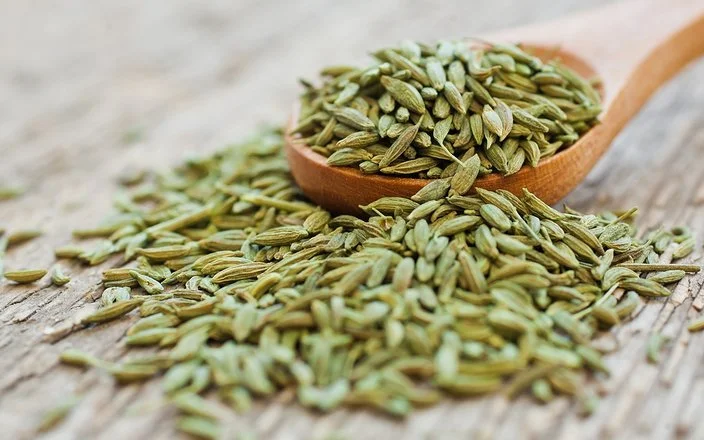 Anissamen liegen auf einem Holzlöffel und auf einem Tisch.