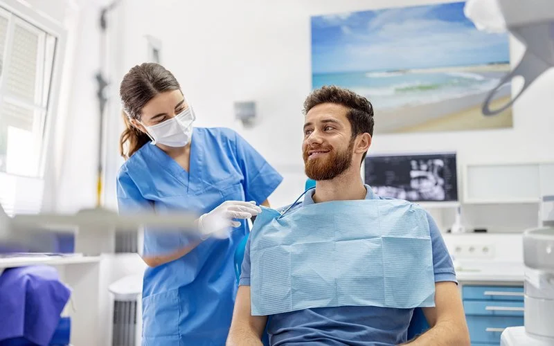 Eine zahnmedizinische Fachkraft bereitet einen Patienten in einer Zahnarztpraxis auf eine Untersuchung oder Behandlung vor.