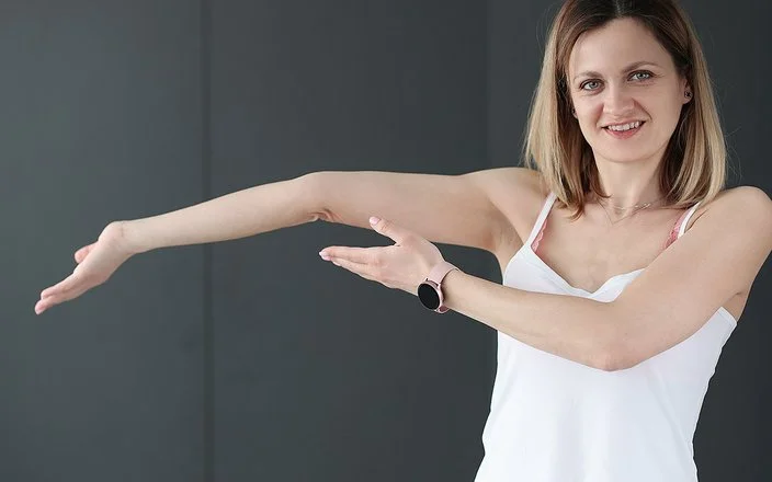 Eine junge Frau zeigt auf ihren überstreckten Arm.